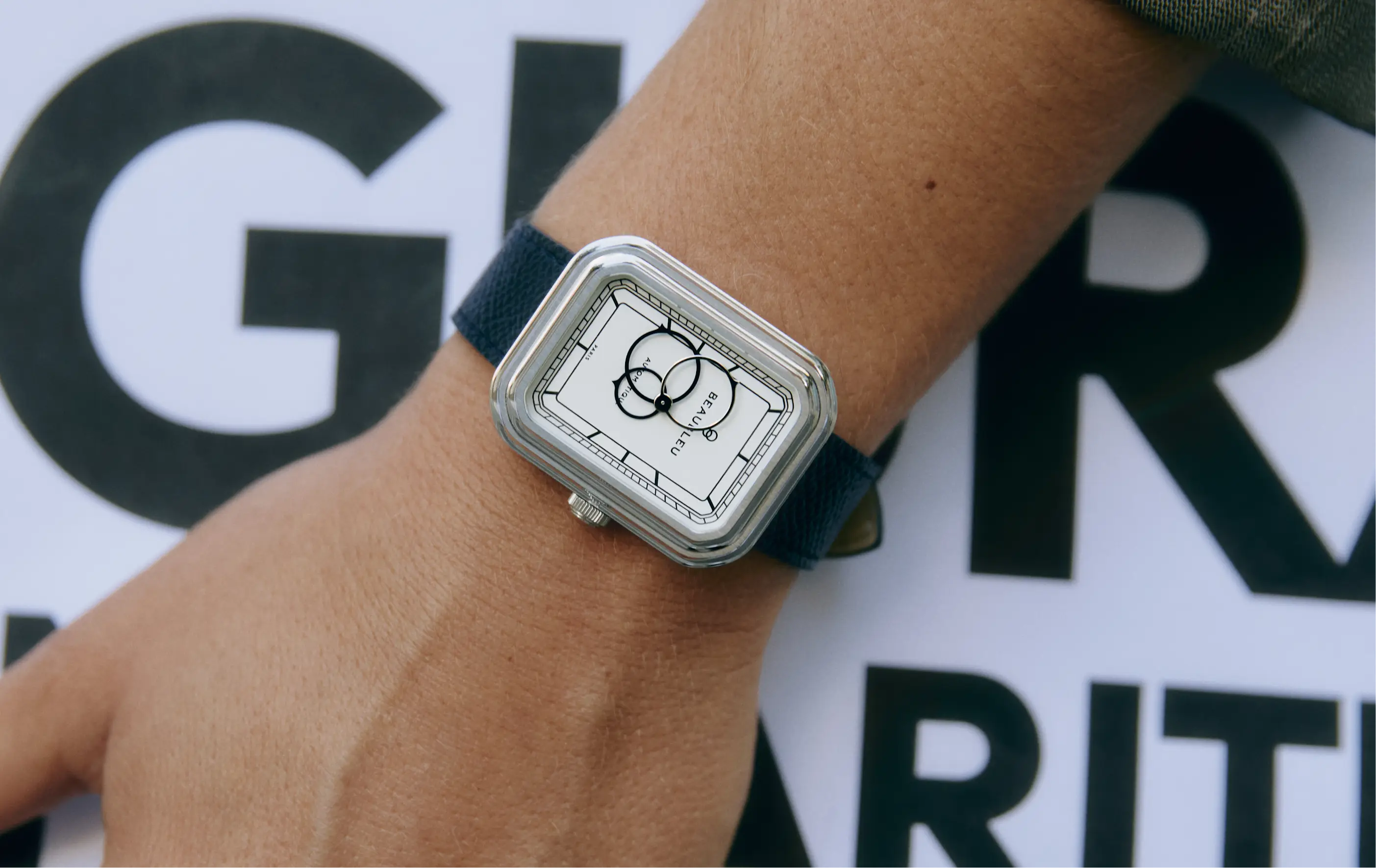 Montre automatique Beaubleu Ecce Figura Alba sur le poignet d'une femme portant un journal