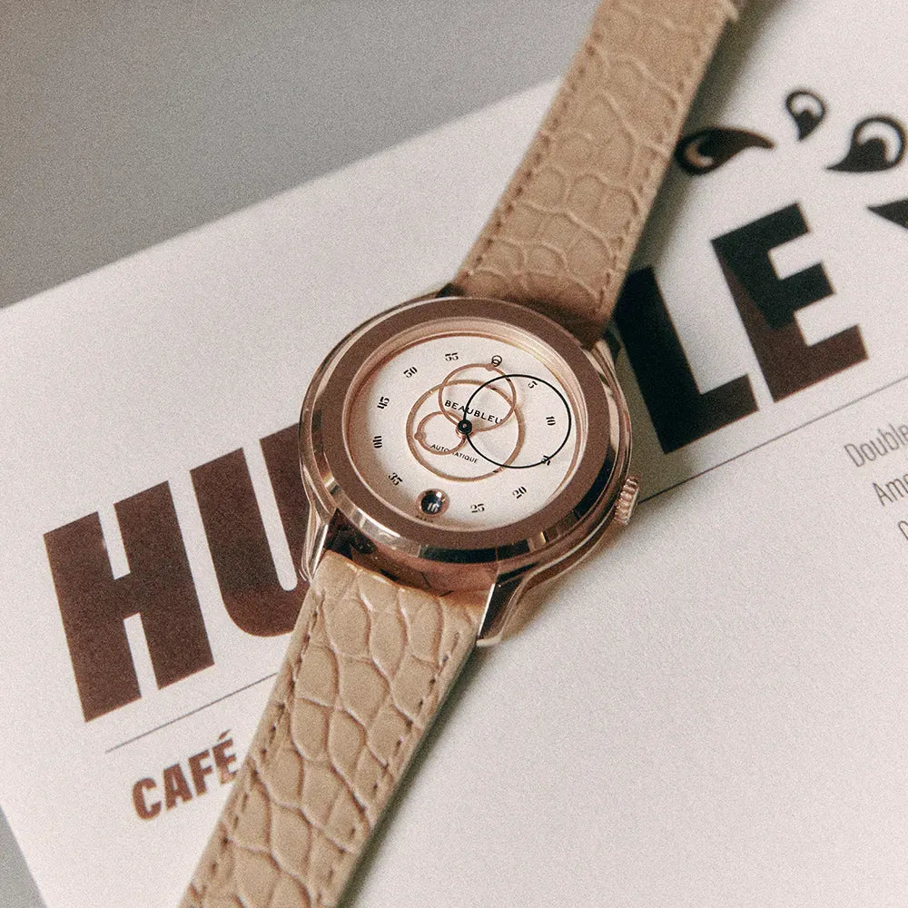 Montre Beaubleu équipée d'un bracelet Flat White en alligator aux écailles rondes, posée sur un magazine.