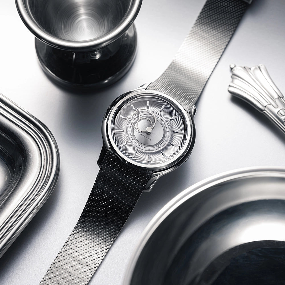 Montre La Pièce Argent de Beaubleu cadran acier posée à côté d'un plateau, verre et couvert en argent