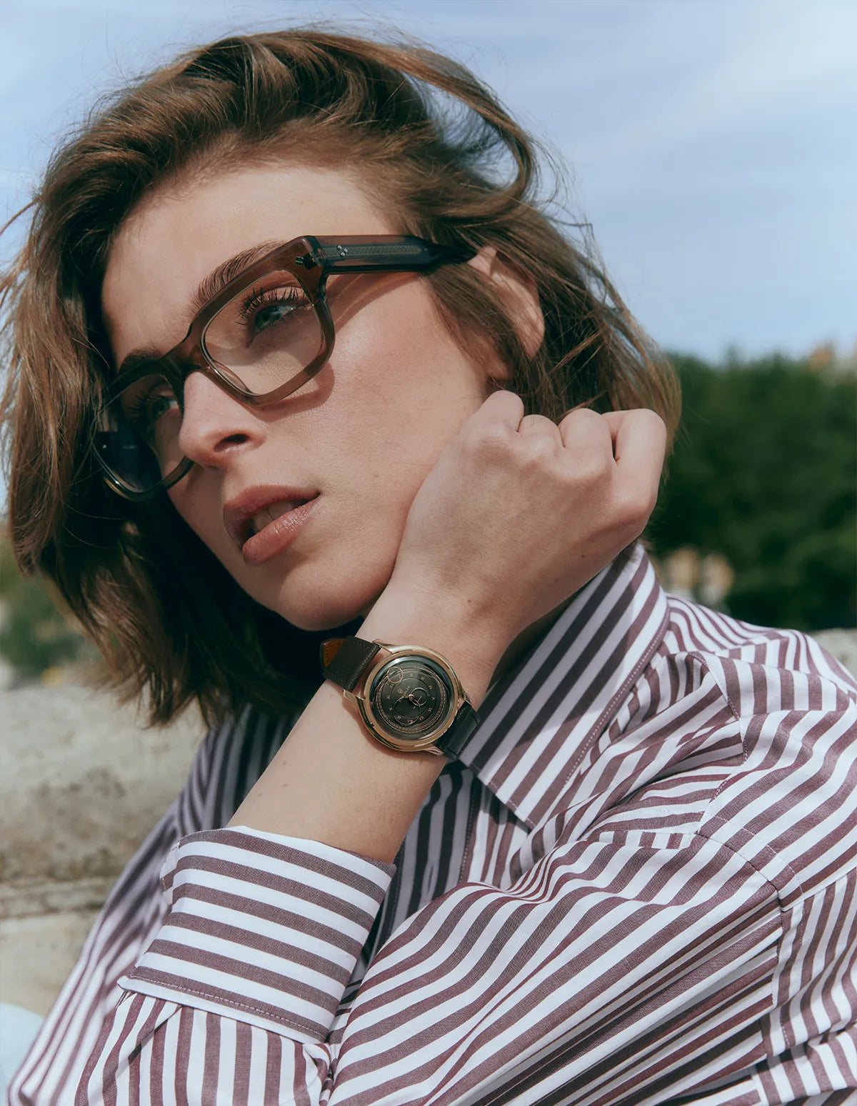 Femme portant des lunettes et une chemise à rayures, mettant en valeur la montre Moka de la collection La Pièce et son cadran couleur marron