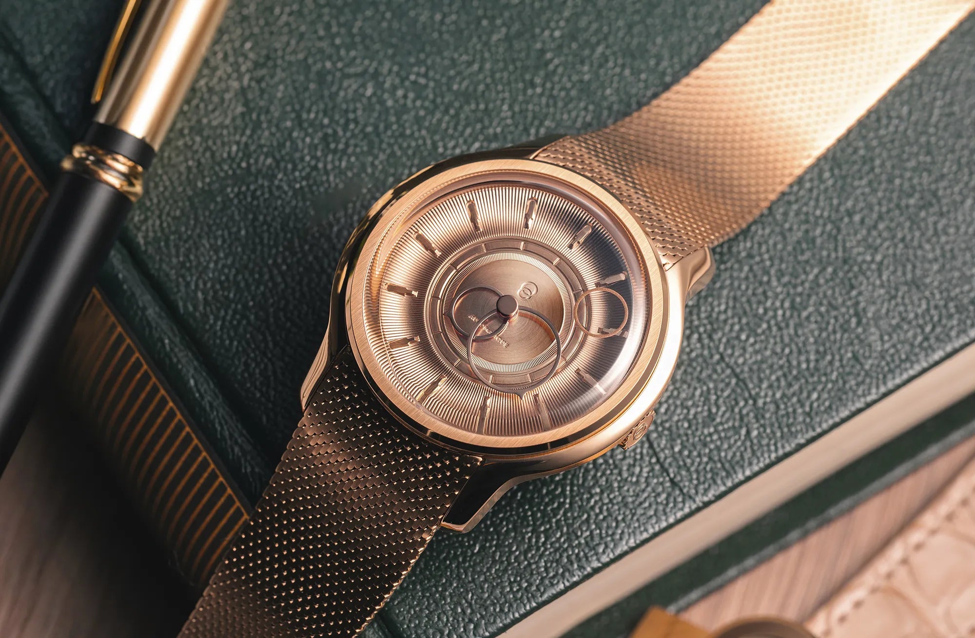 Montre La Pièce Or Rose de Beaubleu cadran or posée sur un carnet avec un stylo à côté