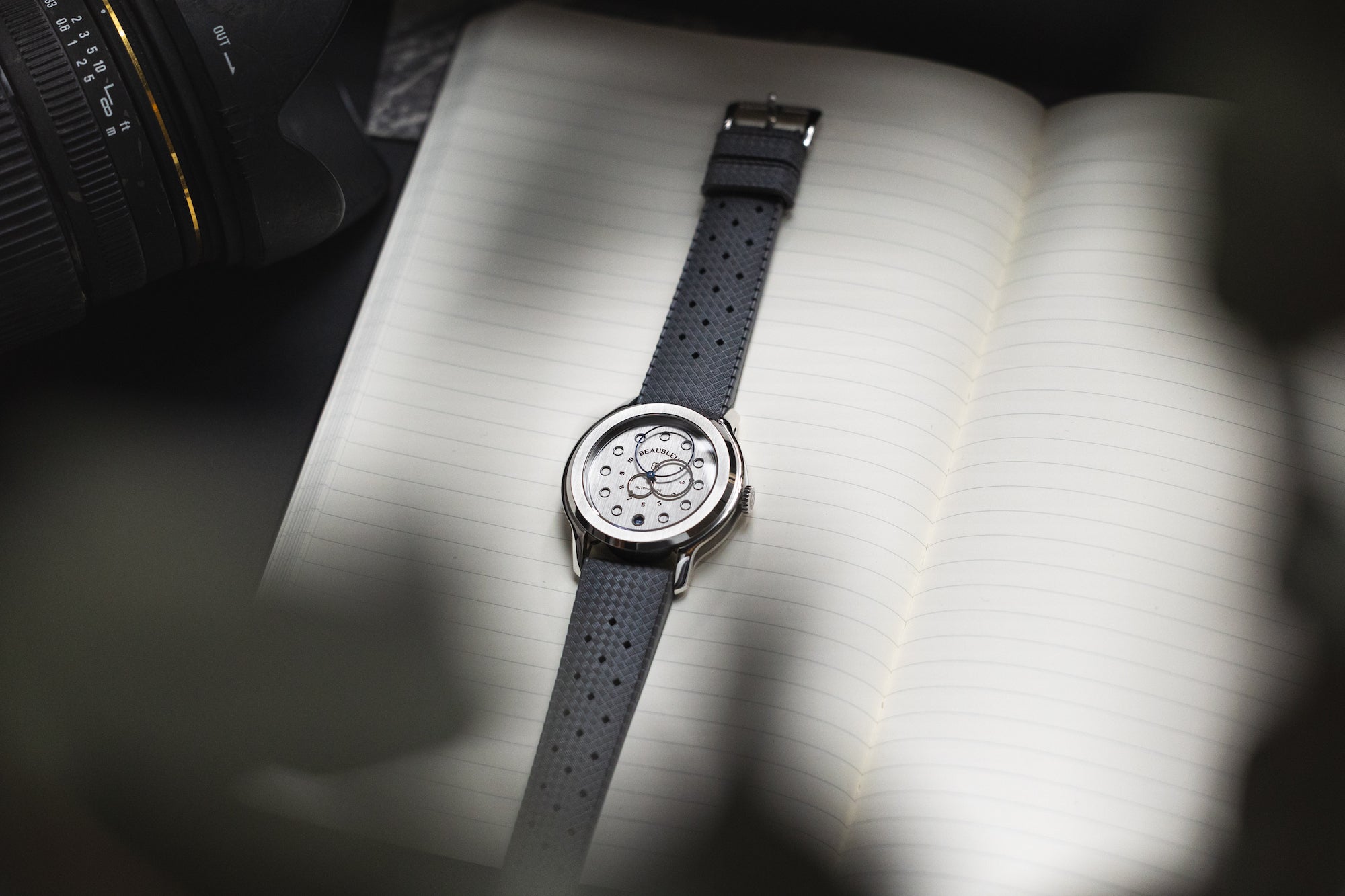 Montre Beaubleu Vitruve Date Acier avec bracelet tropic gris posé sur la page d'un carnet