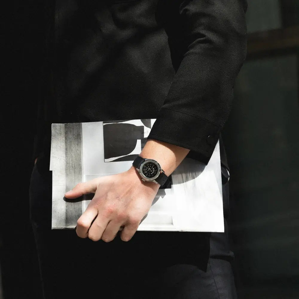 Montre Beaubleu Vitruve Date Noir, avec bracelet en cuir noir, portée au poignet d'un homme tenant un dessin