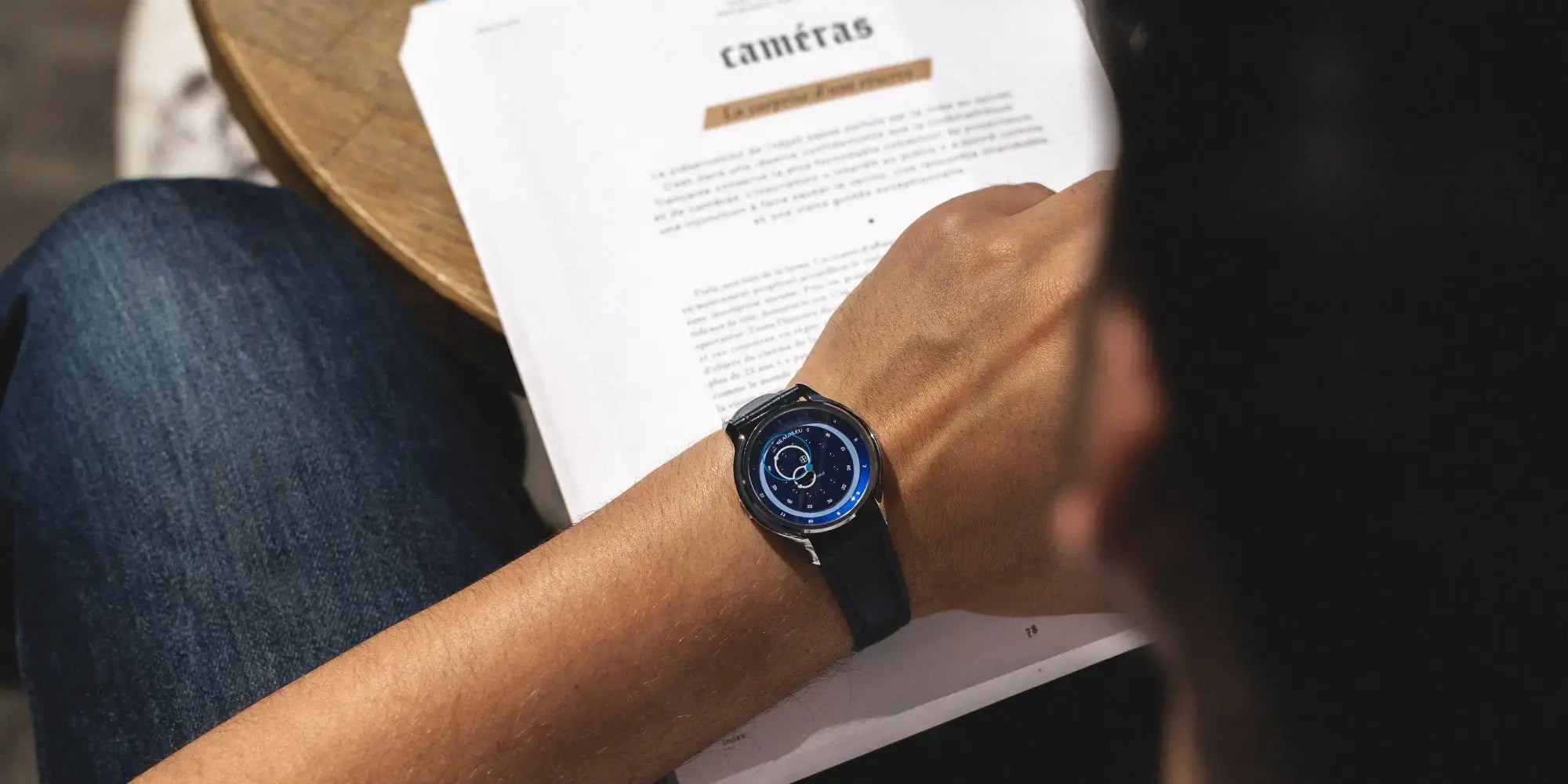 Une montre GMT Bleu avec un bracelet en cuir noir, portée au poignet d'un homme en train de lire un livre
