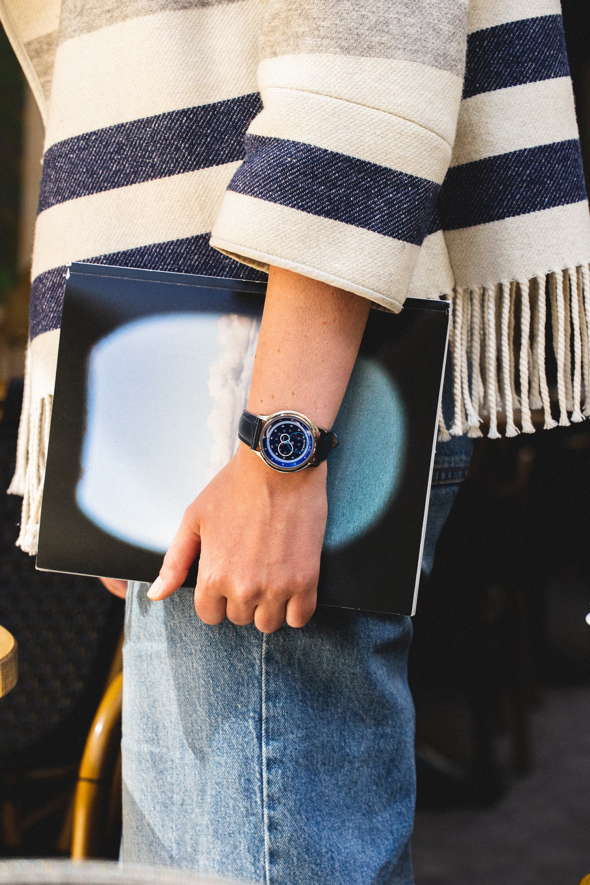 Une montre GMT Bleu avec un bracelet en cuir noir, portée au poignet d'une femme tenant un livre