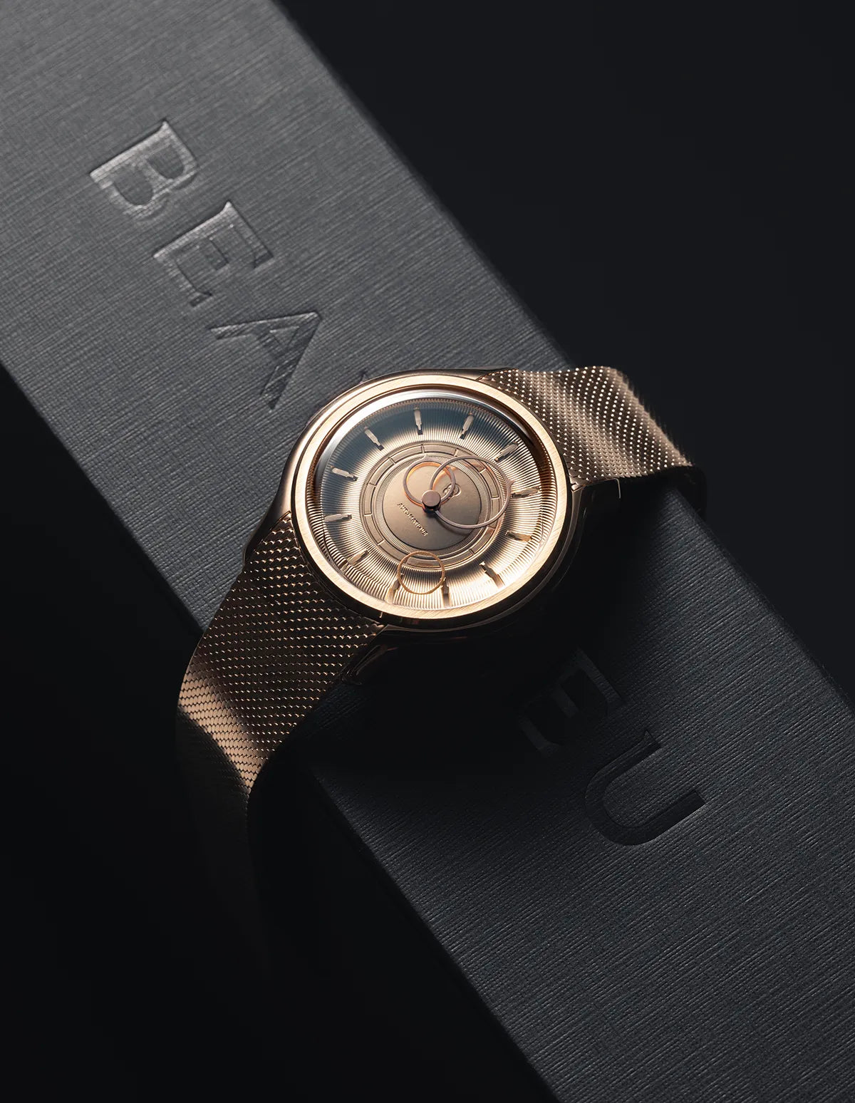 La Pièce Or Rose avec un bracelet maille métallique posée sur un coffret noir de la marque Beaubleu