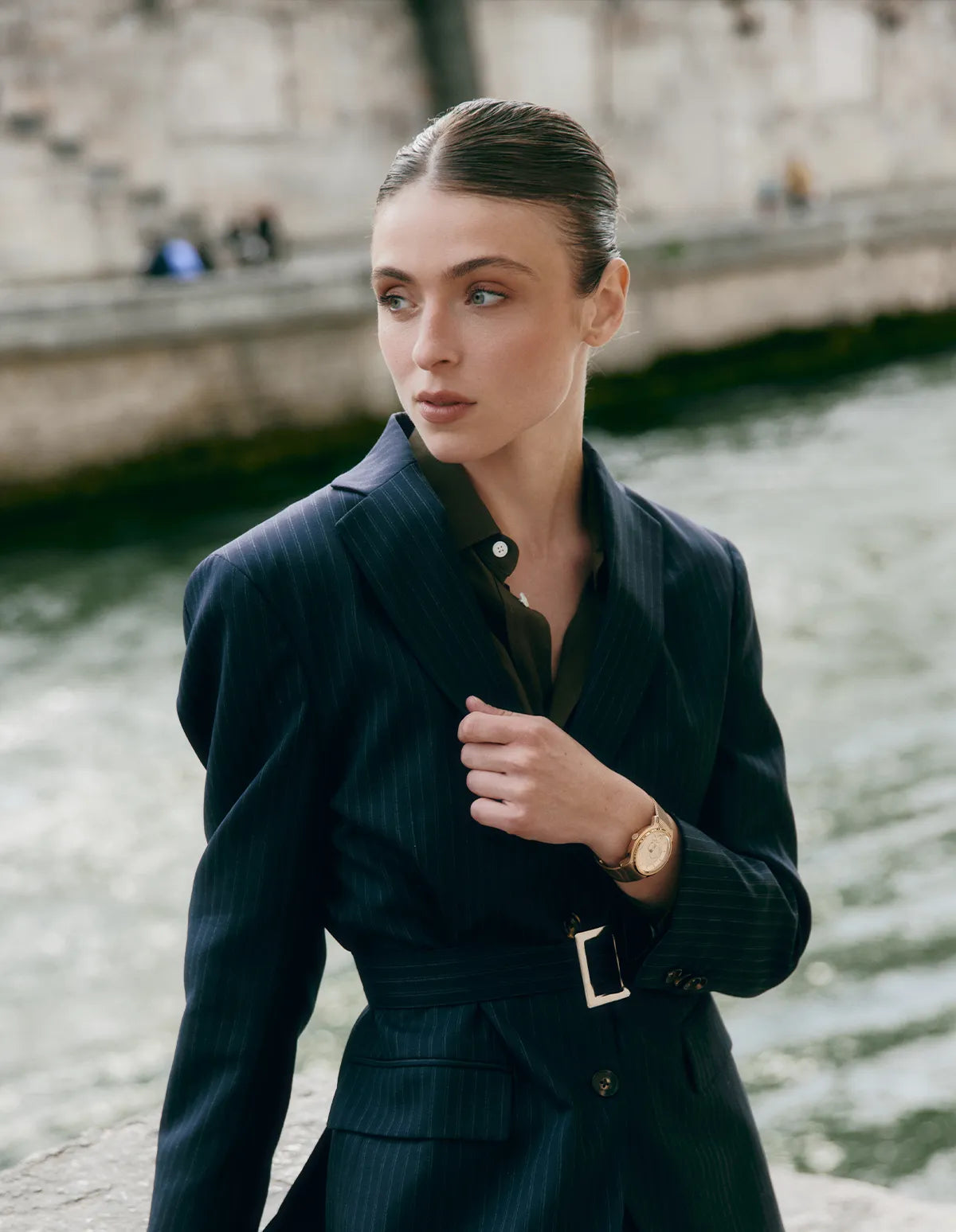 Femme portant un blazer bleu marine et une montre La Pièce Champagne au poignet, photographiée au bord d'un quai