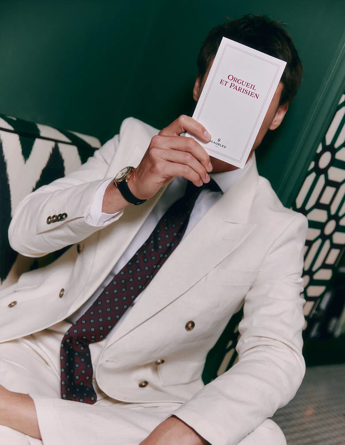 Montre Beaubleu La Pièce Champagne à bracelet en cuir noir grainé portée par un homme en costume blanc assis sur un canapé et tenant un livre dans la main