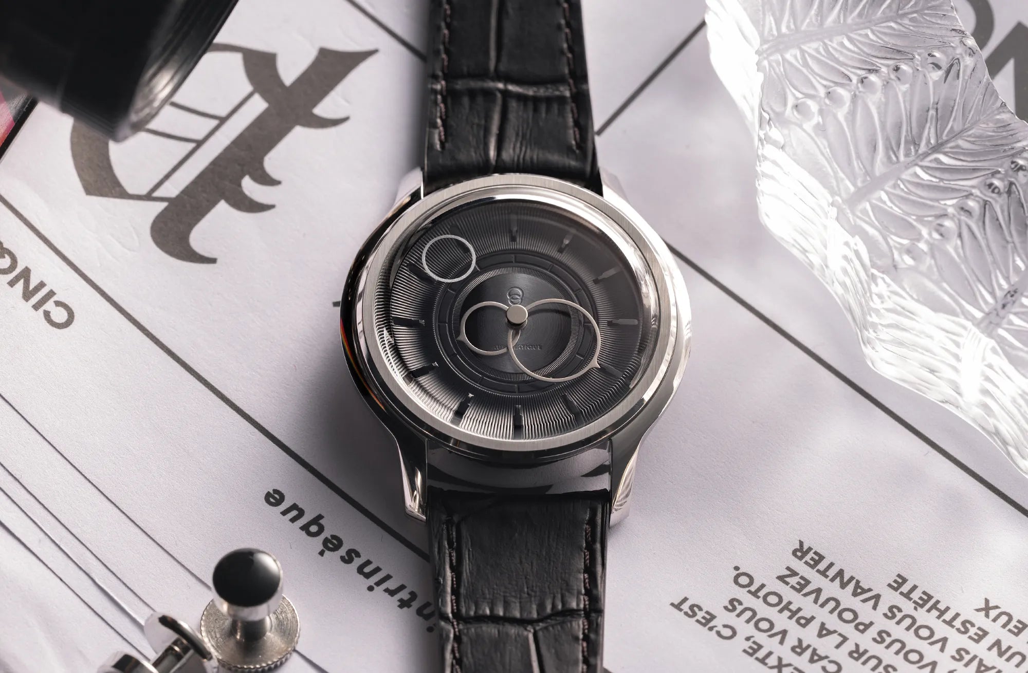 Montre La Pièce Noir de Beaubleu avec bracelet en cuir caiman noir posée sur un journal