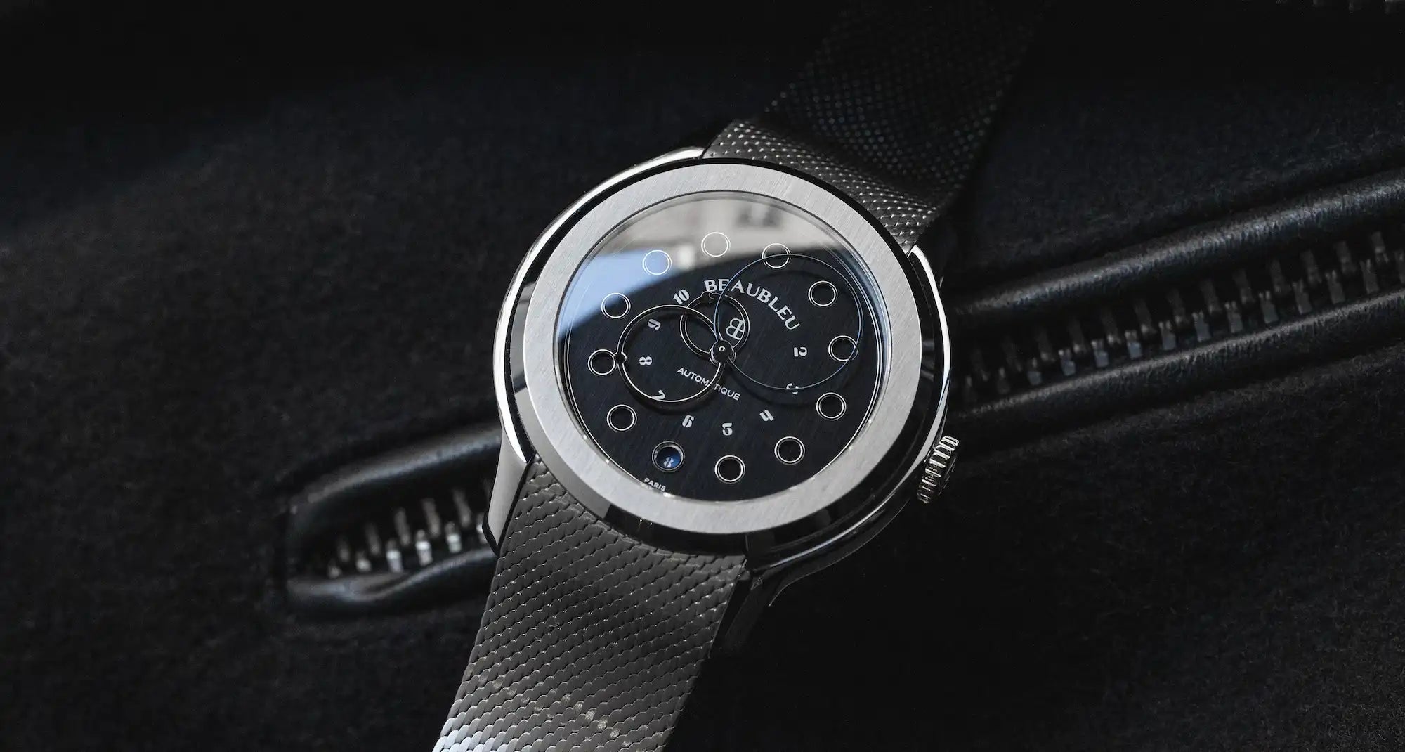 Montre Beaubleu Vitruve Date Noir sur bracelet acier posé sur un fond noir 