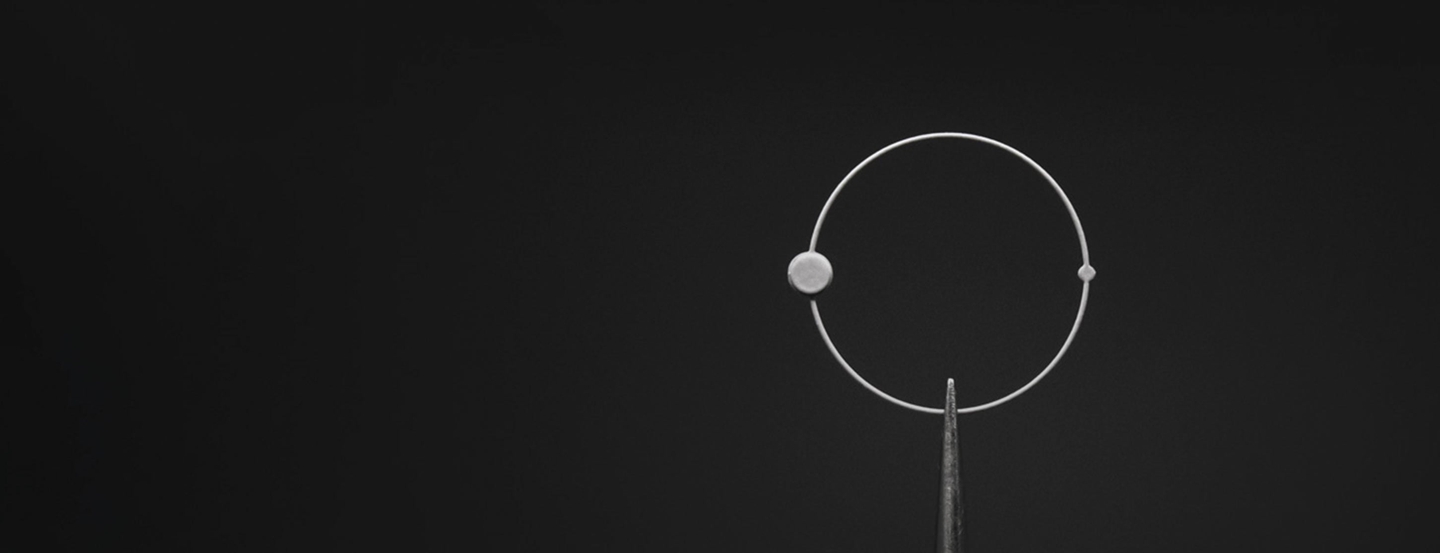 Photo en gros plan d'une aiguille ronde Beaubleu maintenue par une pince d'horloger sur un fond noir