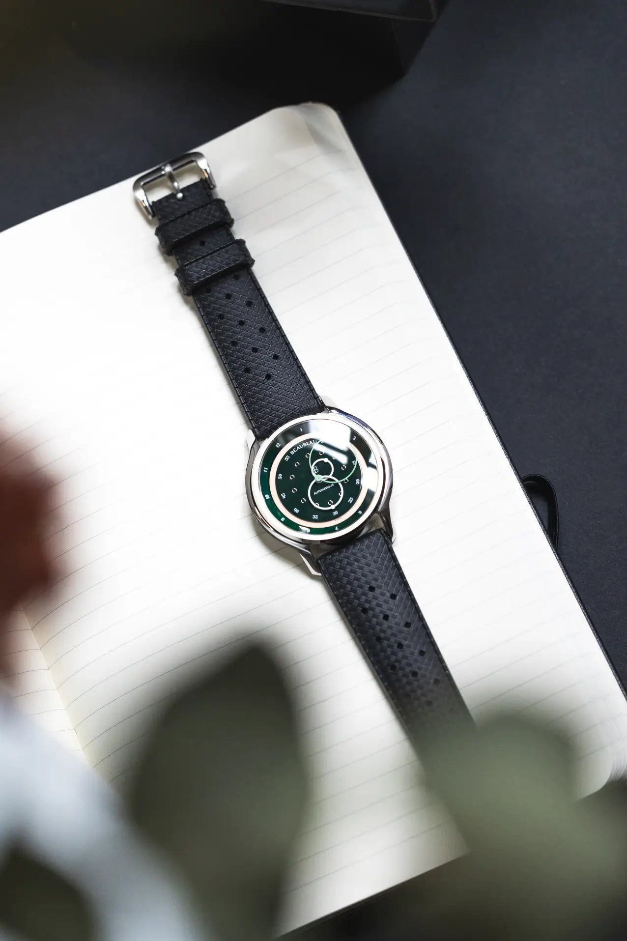 Montre GMT Green avec un bracelet tropic gris, posée sur une page de carnet