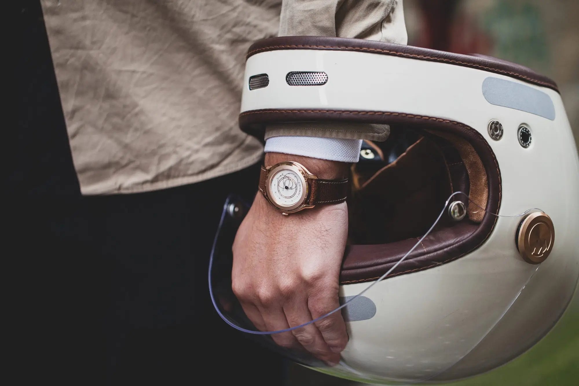 Montre Union Olympe, sur bracelet en cuir grainé cognac, au poignet d'un homme passant sa main à travers un casque de moto vintage blanc