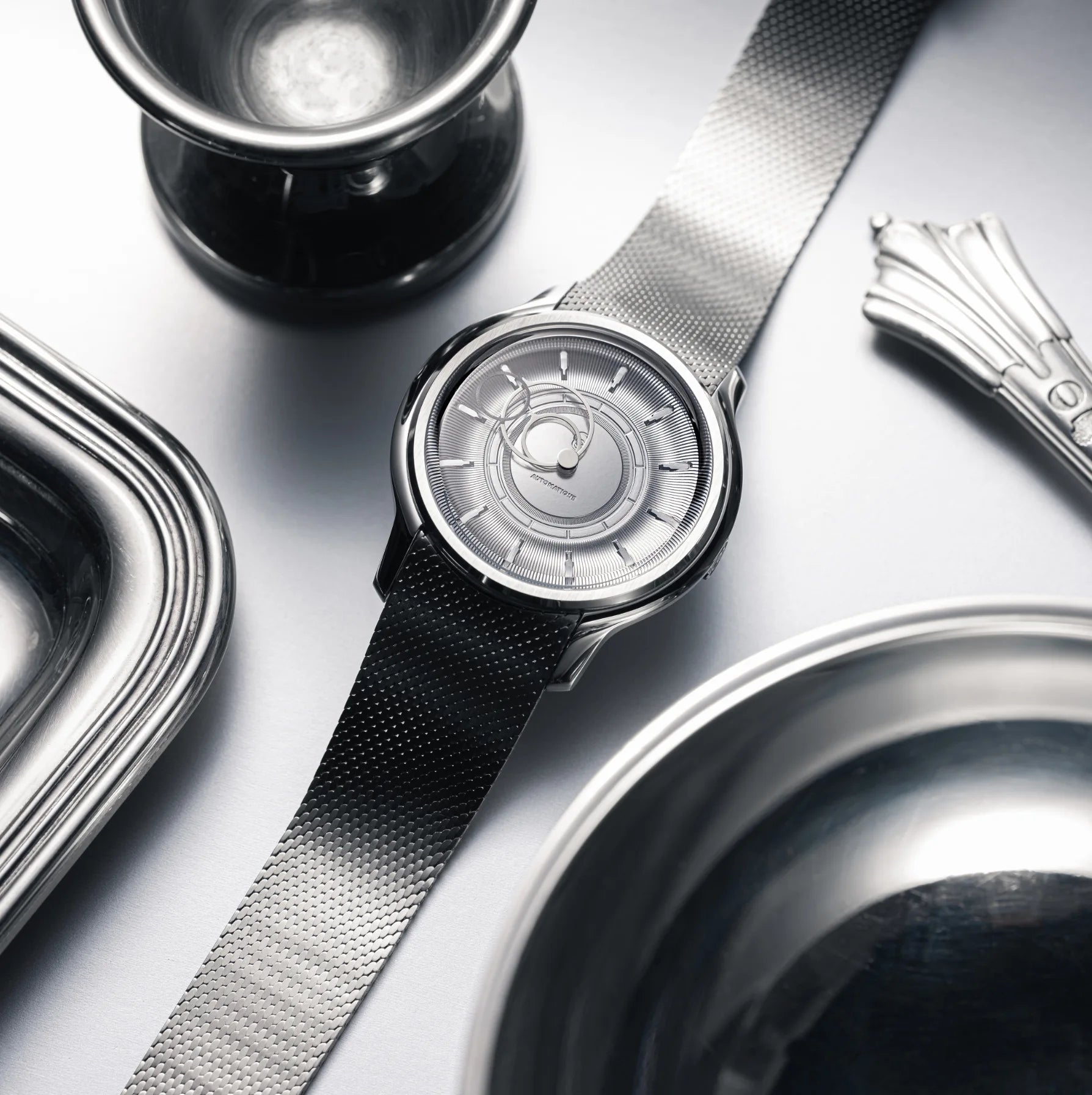 Montre La Pièce Argent de Beaubleu cadran acier posée à côté d'un plateau, verre et couvert en argent