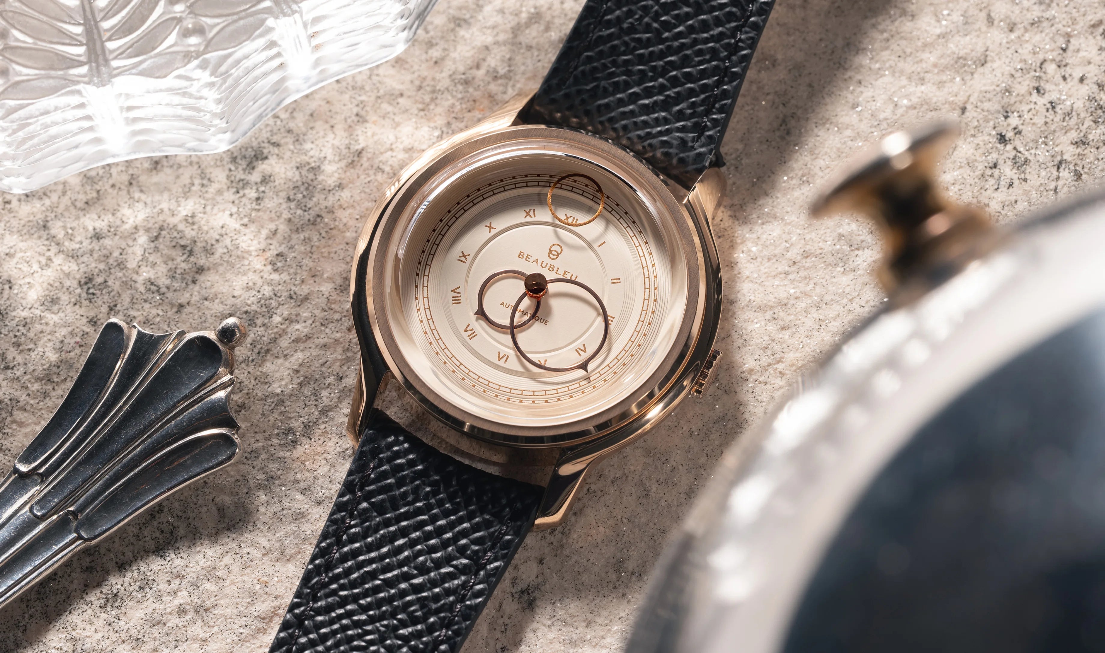 Montre La Pièce Champagne de Beaubleu posée sur du marbre avec à côté un couvert en argent