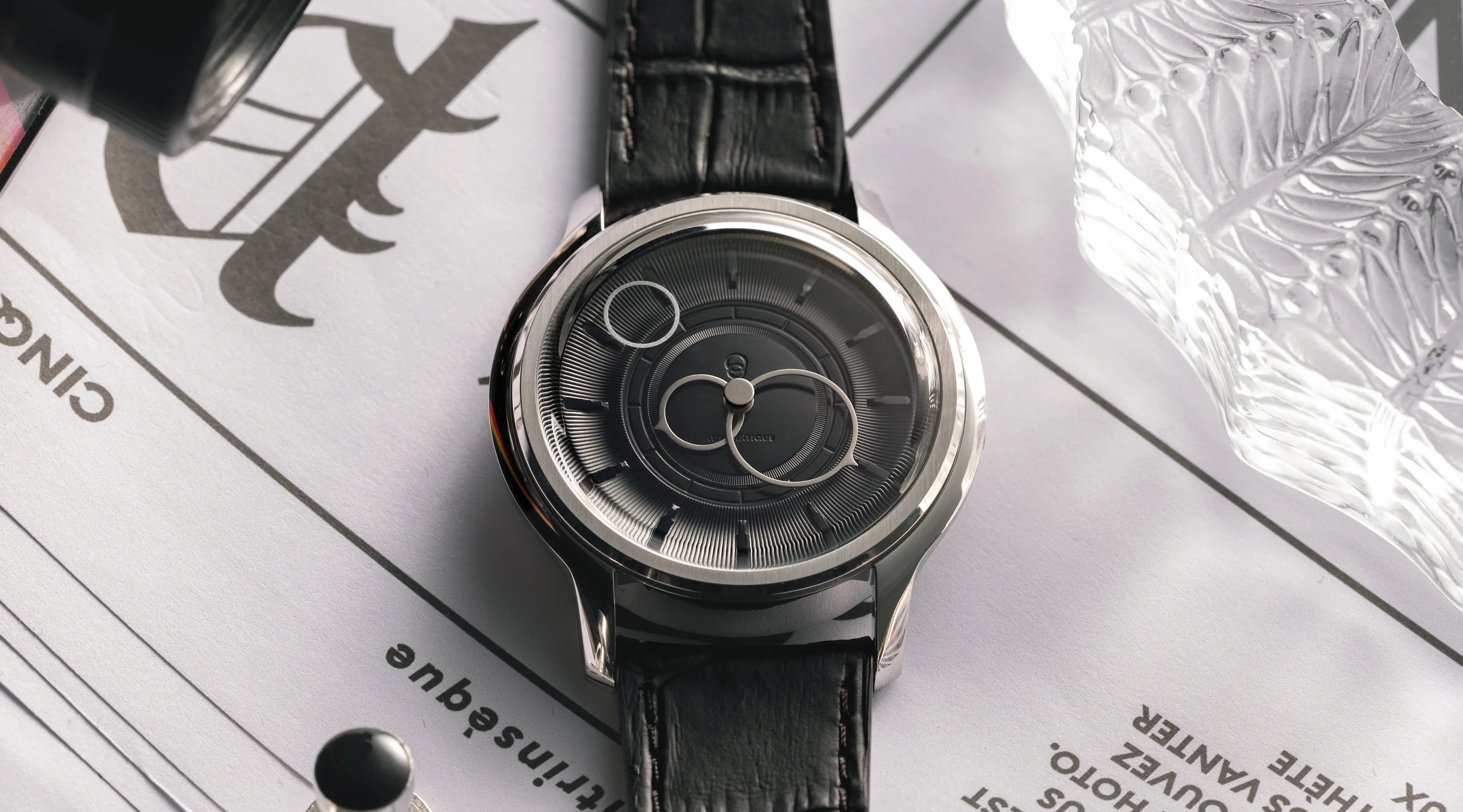 Montre La Pièce Noir de Beaubleu avec bracelet en cuir caiman noir posée sur un journal