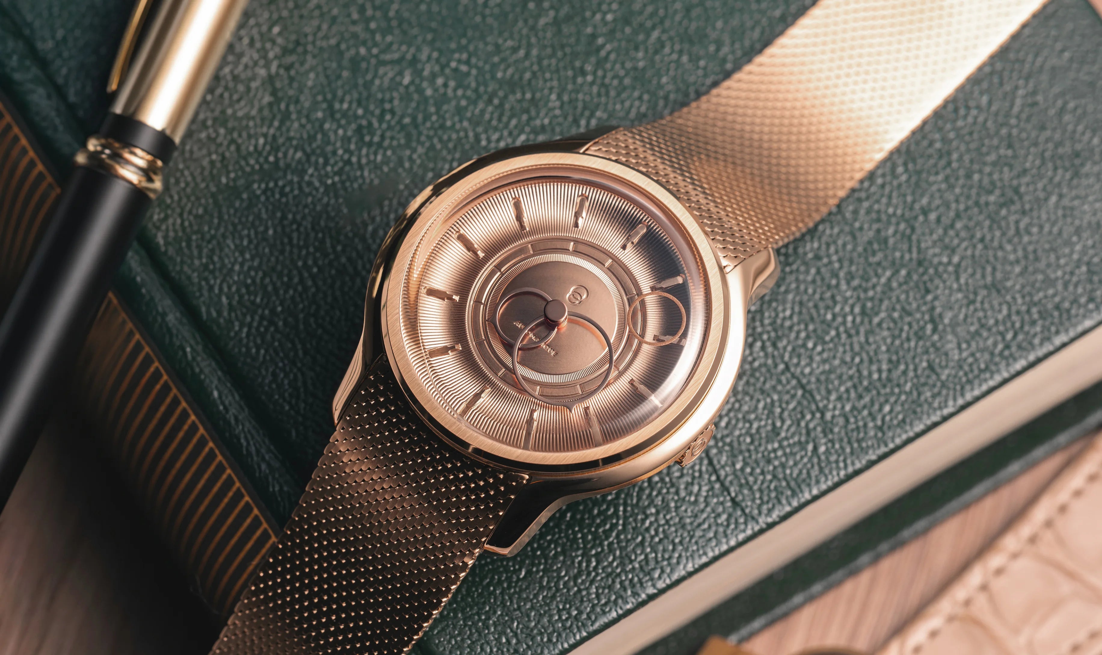 Montre La Pièce Or Rose de Beaubleu cadran or posée sur un carnet avec un stylo à côté